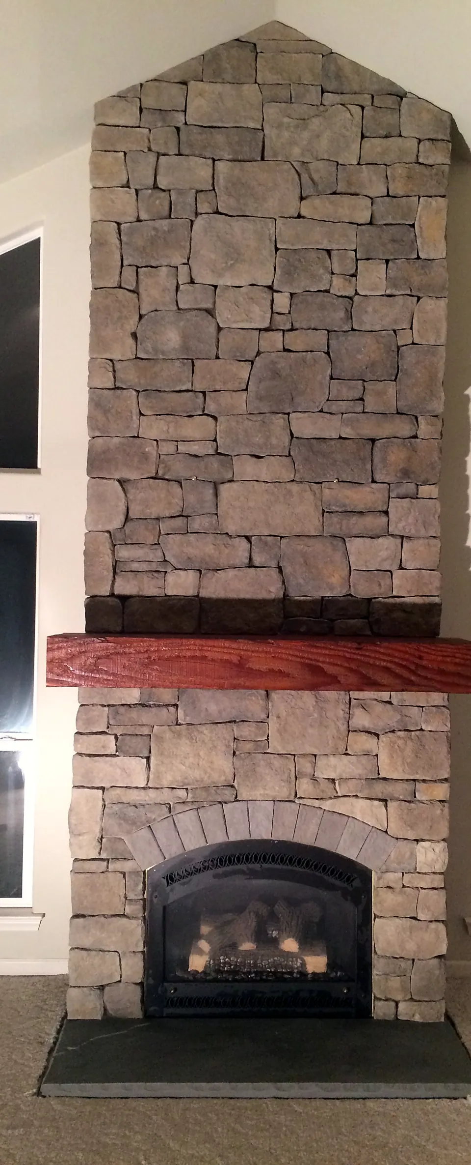 Stone fireplace rising to a vaulted ceiling between tall windows, with an arched firebox surround and wood mantel