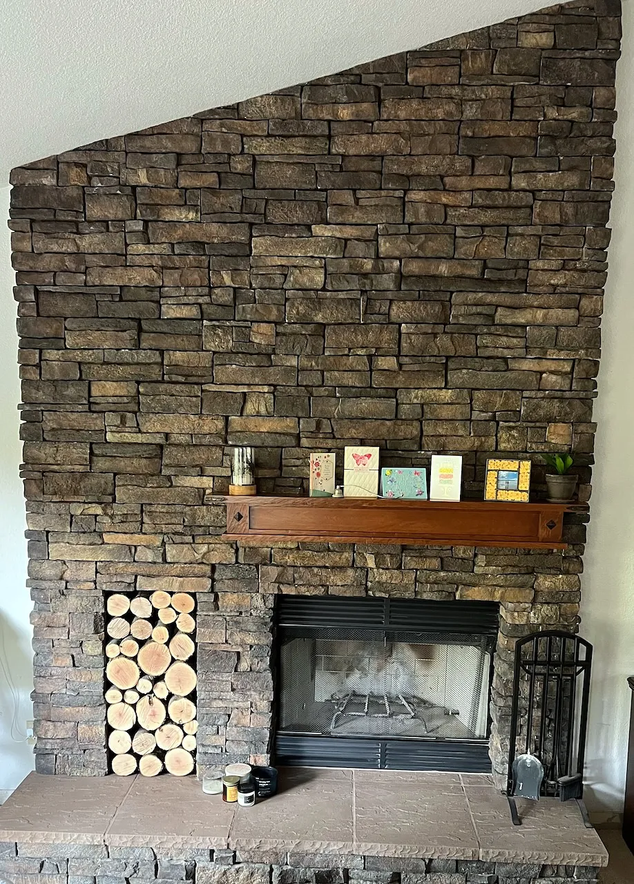 Dark stacked stone fireplace rising to a vaulted ceiling with a wood mantel and a firewood niche